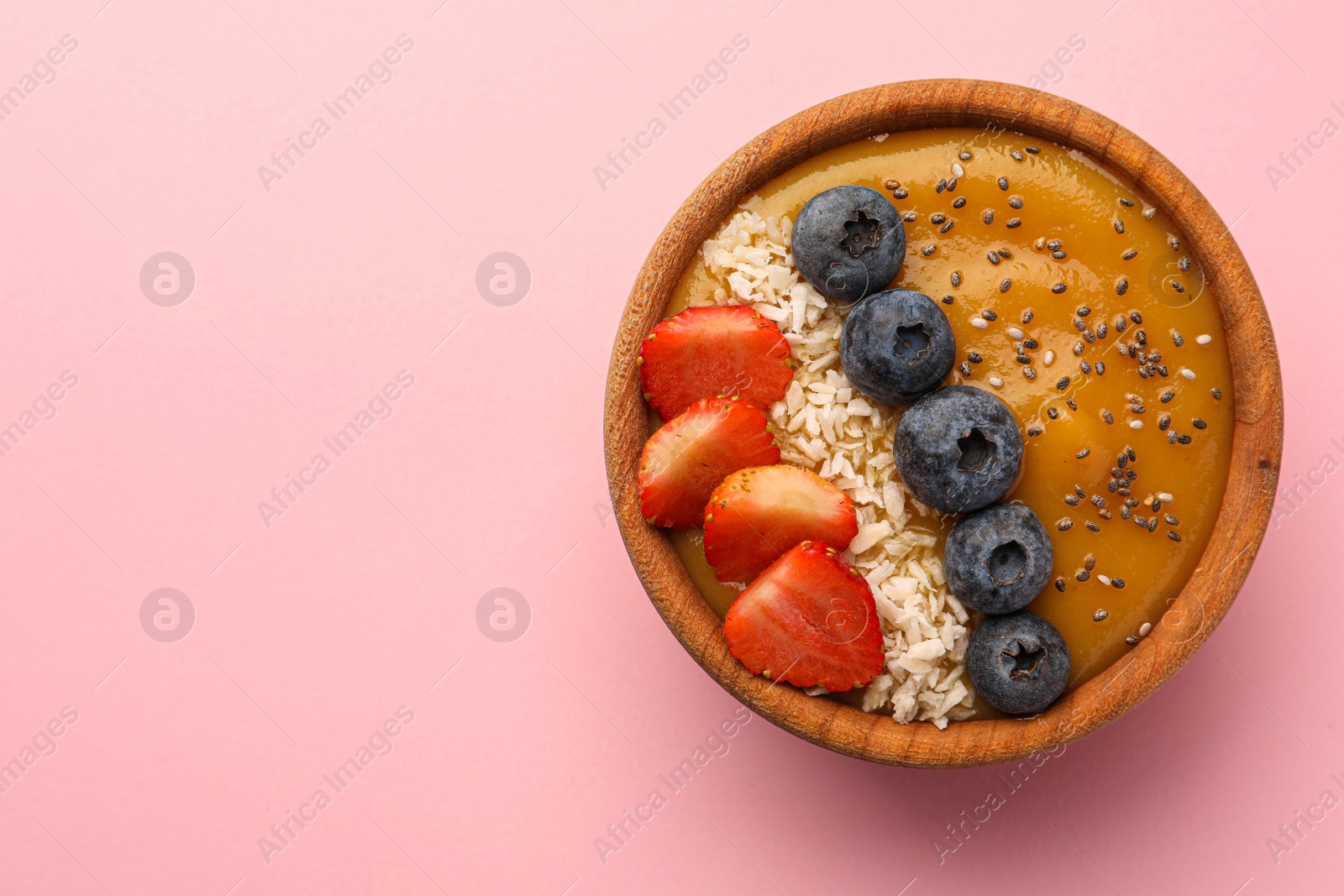 Photo of Delicious smoothie bowl with fresh berries, chia seeds and coconut flakes on pale pink background, top view. Space for text
