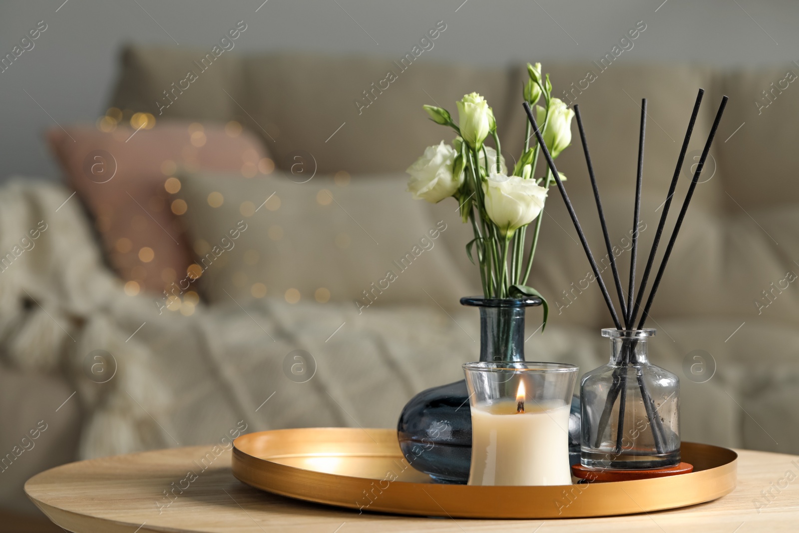 Photo of Burning candle with oil reed diffuser and bouquet on wooden table in living room. Space for text