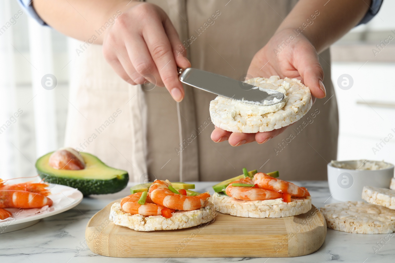 Photo of Woman spreading butter on puffed rice cake over white table indoors, closeup