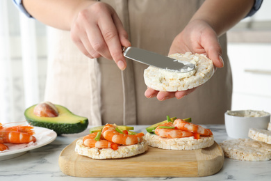 Woman spreading butter on puffed rice cake over white table indoors, closeup