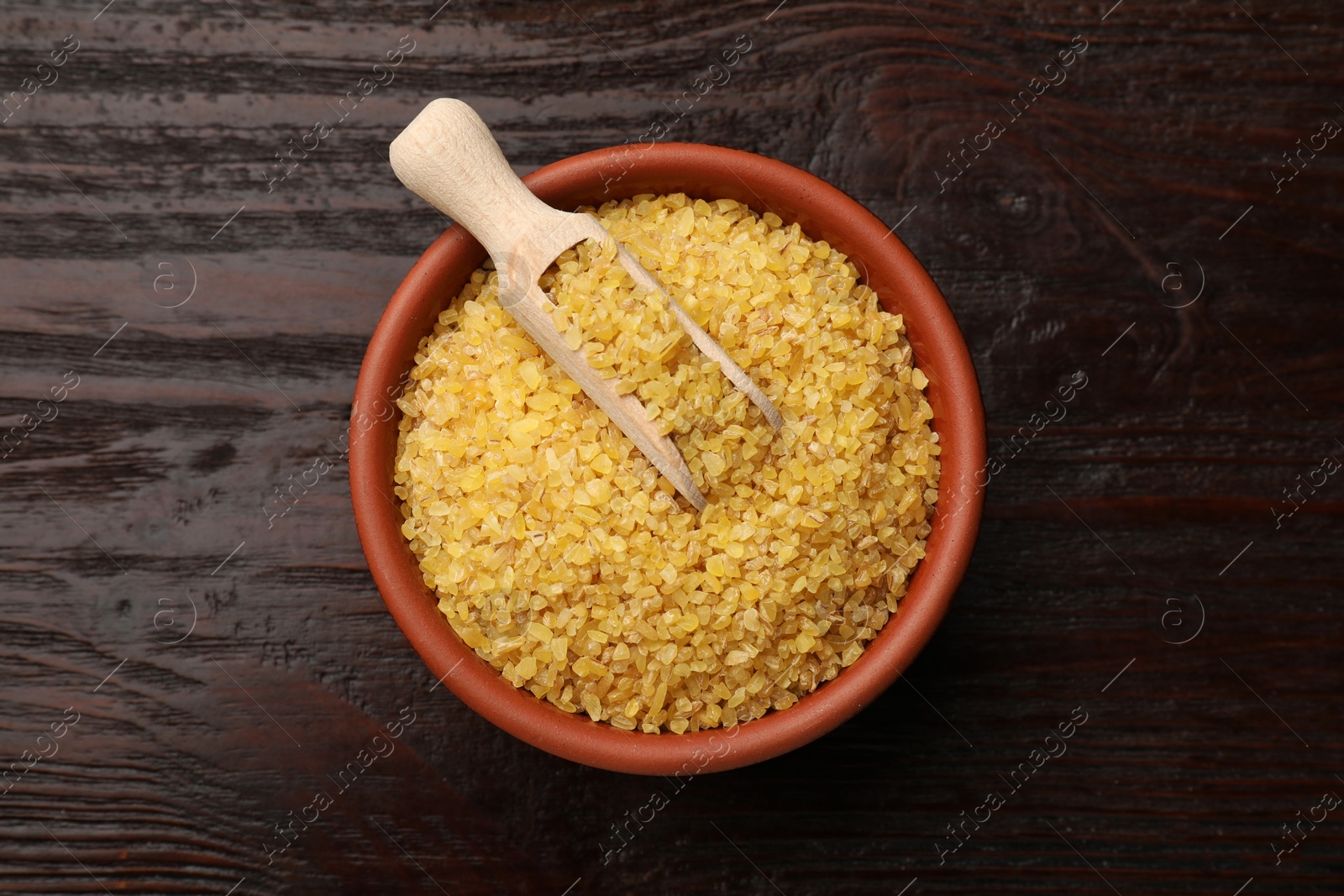 Photo of Bowl and scoop with raw bulgur on wooden table, top view