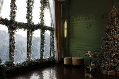 Photo of Beautiful Christmas tree and windows decorated with garlands and lights indoors. Interior design