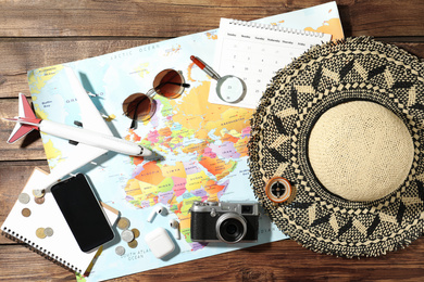 World map and items on wooden background, flat lay. Travel during summer vacation