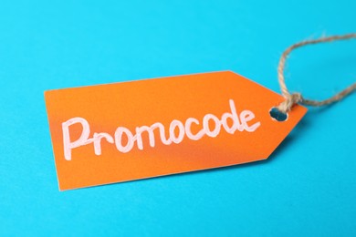 Photo of Tag with words Promo Code on light blue background, closeup