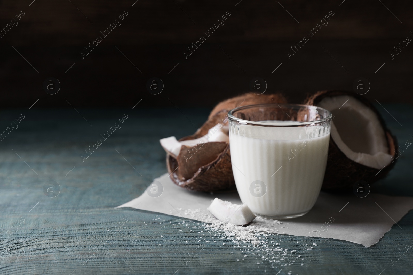 Photo of Glass of delicious coconut milk, flakes and nuts on wooden table, space for text