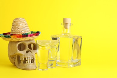 Human scull with Mexican sombrero hat, tequila and lime on yellow background