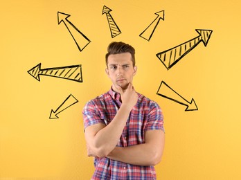 Image of Choice in profession or other areas of life, concept. Making decision, thoughtful young man surrounded by drawn arrows on yellow background