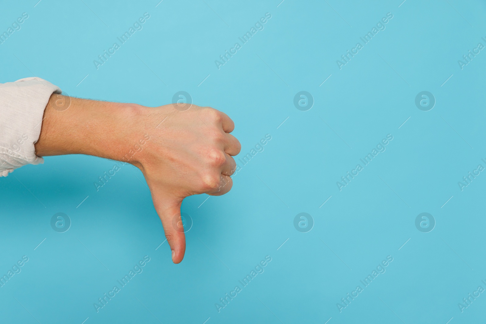 Photo of Man showing thumb down on light blue background, closeup. Space for text