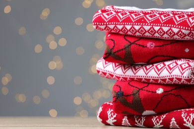 Photo of Stack of different Christmas sweaters on table against grey background with blurred lights. Space for text