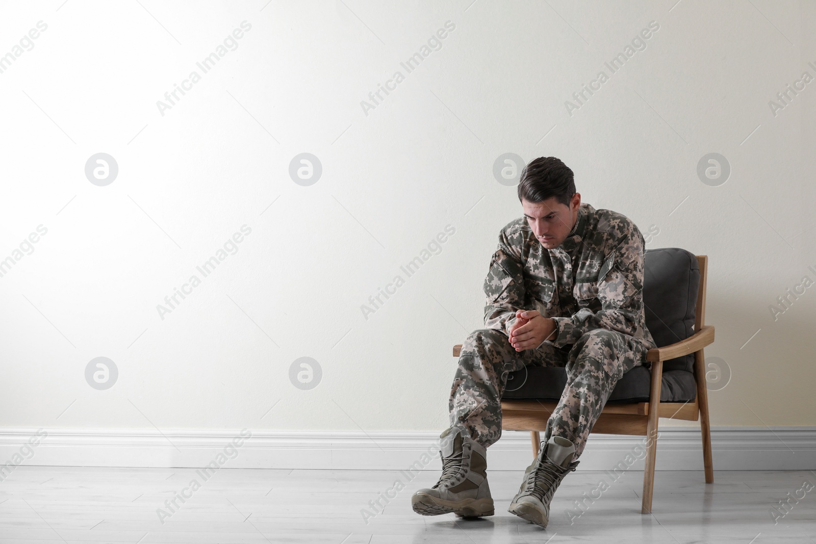 Photo of Stressed military officer sitting in armchair near white wall indoors. Space for text