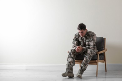 Stressed military officer sitting in armchair near white wall indoors. Space for text