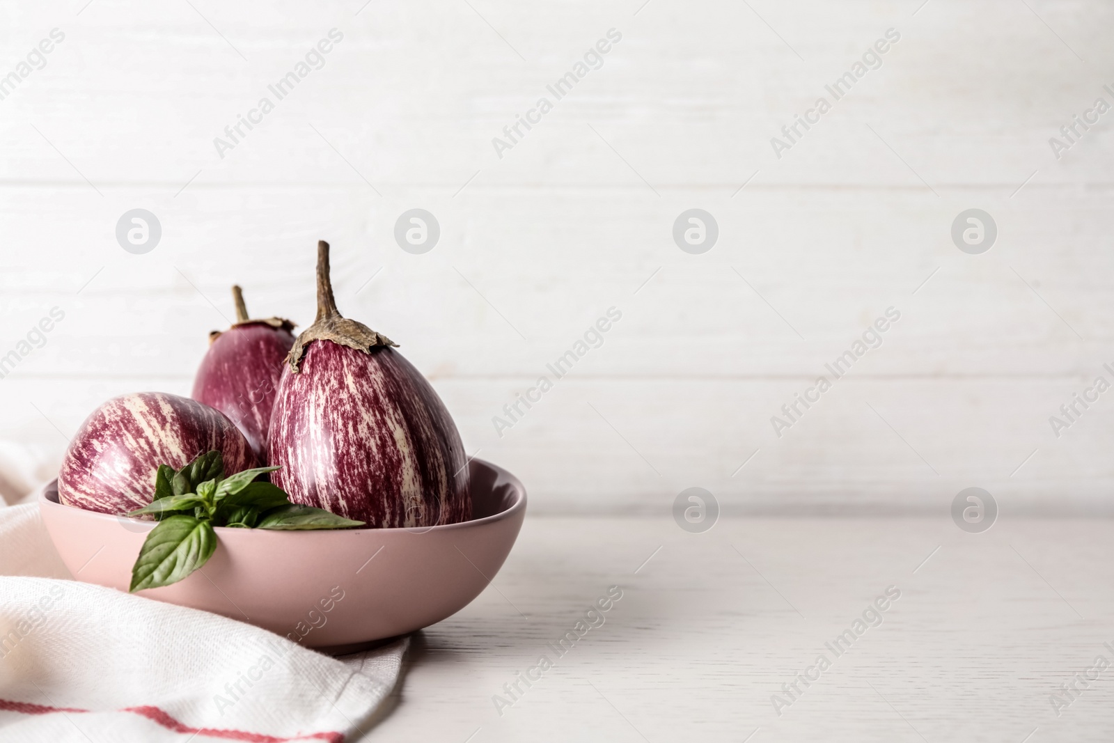 Photo of Ripe purple eggplants and basil on white table. Space for text