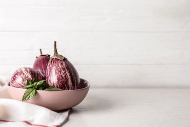 Photo of Ripe purple eggplants and basil on white table. Space for text