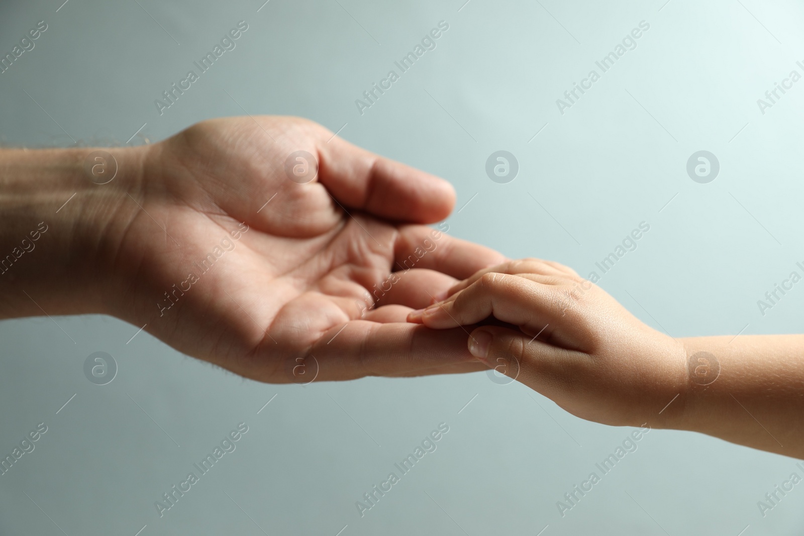 Photo of Father and child holding hands on light blue background, closeup