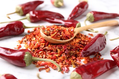 Photo of Chili pepper flakes and pods on white marble table, closeup