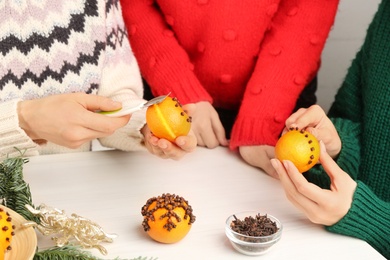 Friends decorating fresh tangerines with cloves at light wooden table, closeup. Making Christmas pomander balls