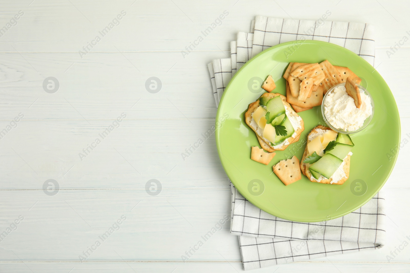 Photo of Delicious crackers with cream cheese, cucumber and parsley on white wooden table, top view. Space for text