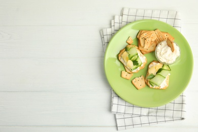 Delicious crackers with cream cheese, cucumber and parsley on white wooden table, top view. Space for text