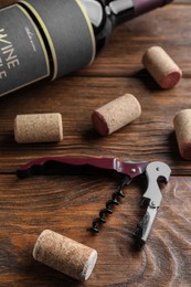 Photo of Corkscrew, wine bottle and stoppers on wooden table.