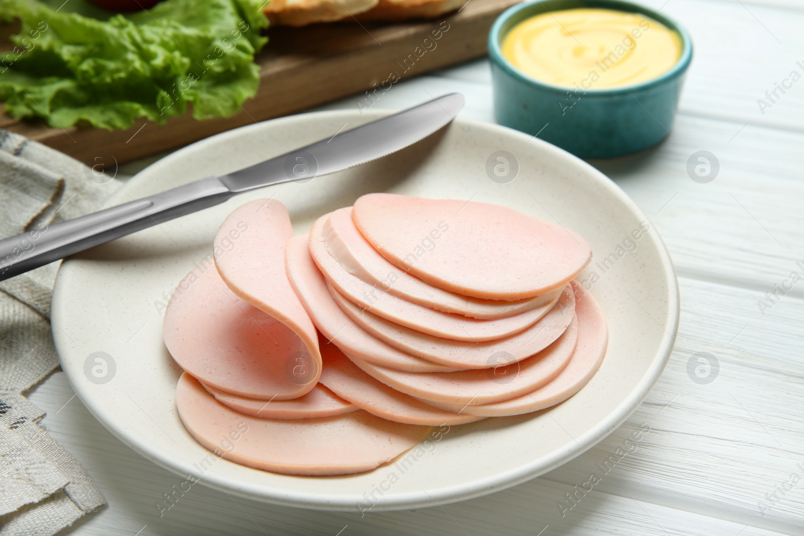 Photo of Slices of delicious boiled sausage served on white wooden table, closeup