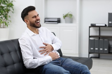 Photo of Handsome young man laughing on sofa in office
