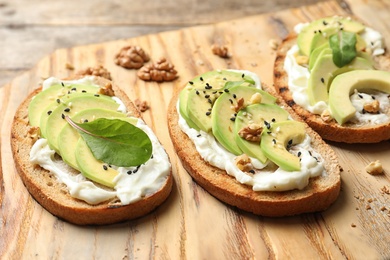 Photo of Delicious bruschettas with avocado served on wooden board, closeup