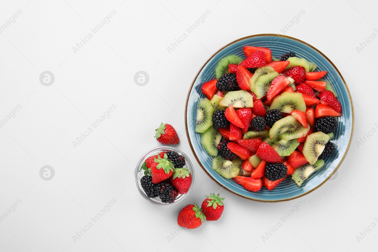 Photo of Plate of fruit salad and ingredients on light background, flat lay. Space for text