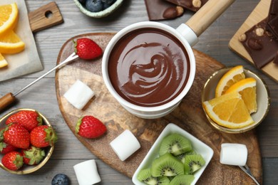 Flat lay composition with fondue pot of melted chocolate on wooden table