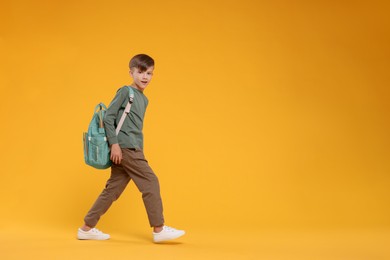 Photo of Cute schoolboy walking on orange background, space for text