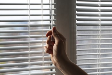 Man opening white blinds at home, closeup