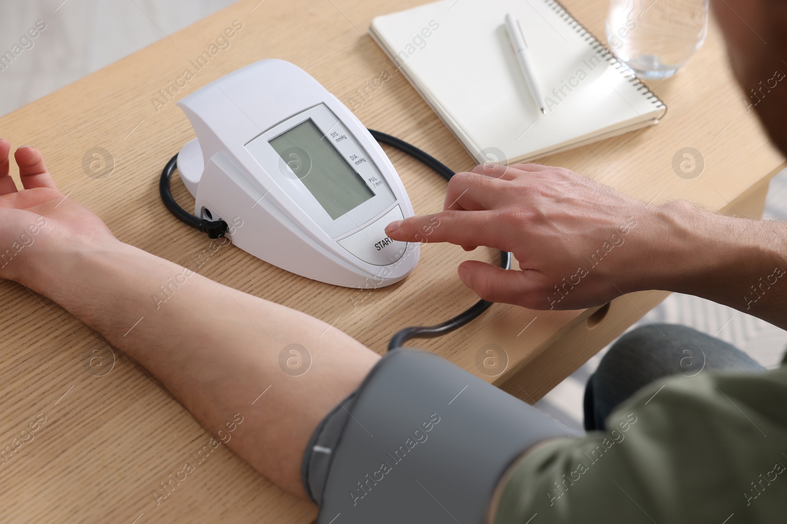 Photo of Man measuring blood pressure at wooden table in room, closeup