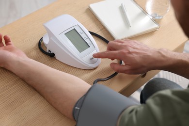 Photo of Man measuring blood pressure at wooden table in room, closeup