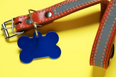 Leather dog collar with blue tag in shape of bone on yellow background, closeup. Space for text