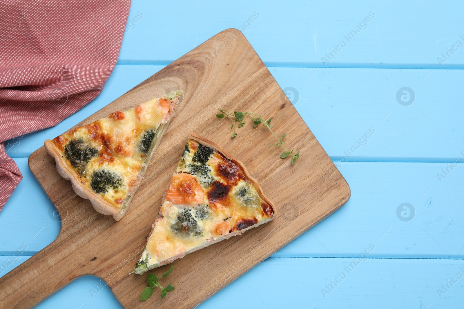 Photo of Delicious homemade quiche with salmon and broccoli on light blue wooden table, top view. Space for text