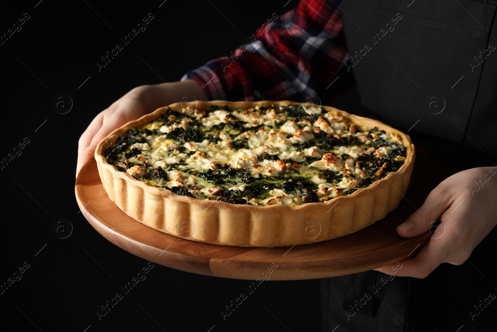 Photo of Woman holding delicious homemade spinach quiche on dark background, closeup