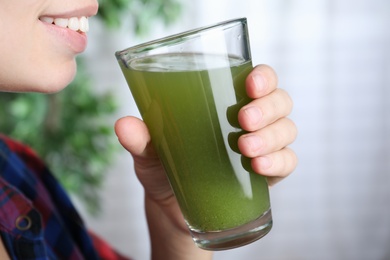 Woman holding glass with fresh celery juice indoors, closeup