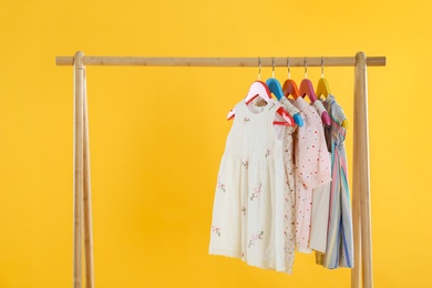 Rack with stylish children clothes on yellow background