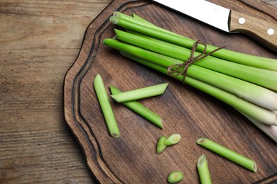 Photo of Fresh lemongrass, knife and cutting board on wooden table, top view