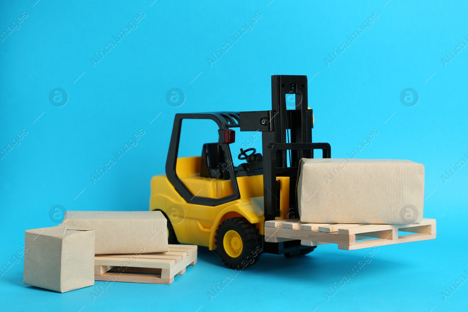 Photo of Toy forklift, wooden pallets and boxes on light blue background