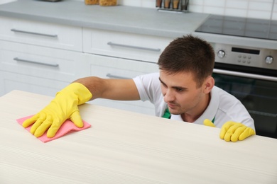 Photo of Man cleaning table with rag in kitchen