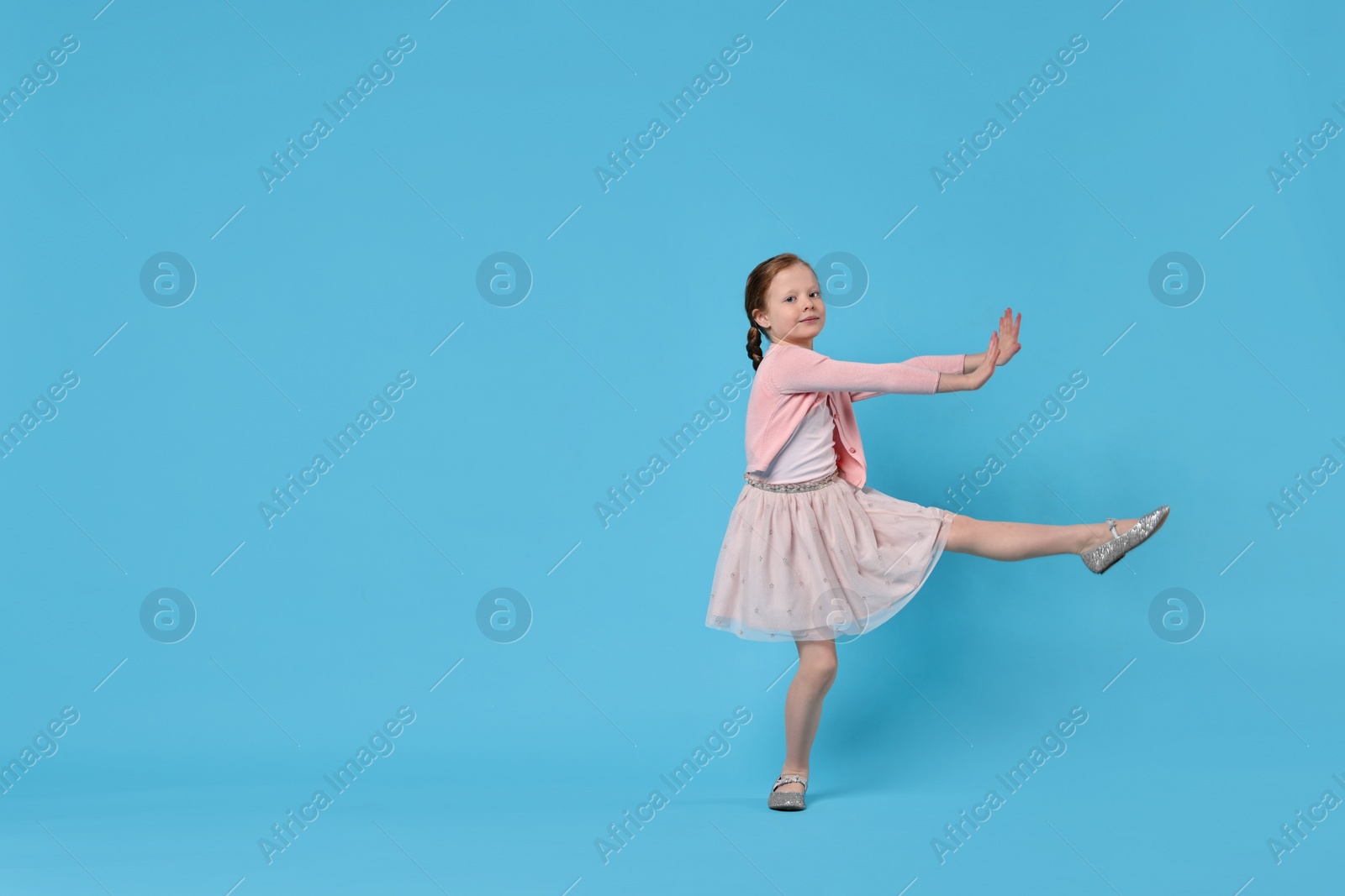 Photo of Cute little girl dancing on light blue background, space for text