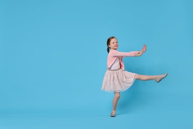 Cute little girl dancing on light blue background, space for text