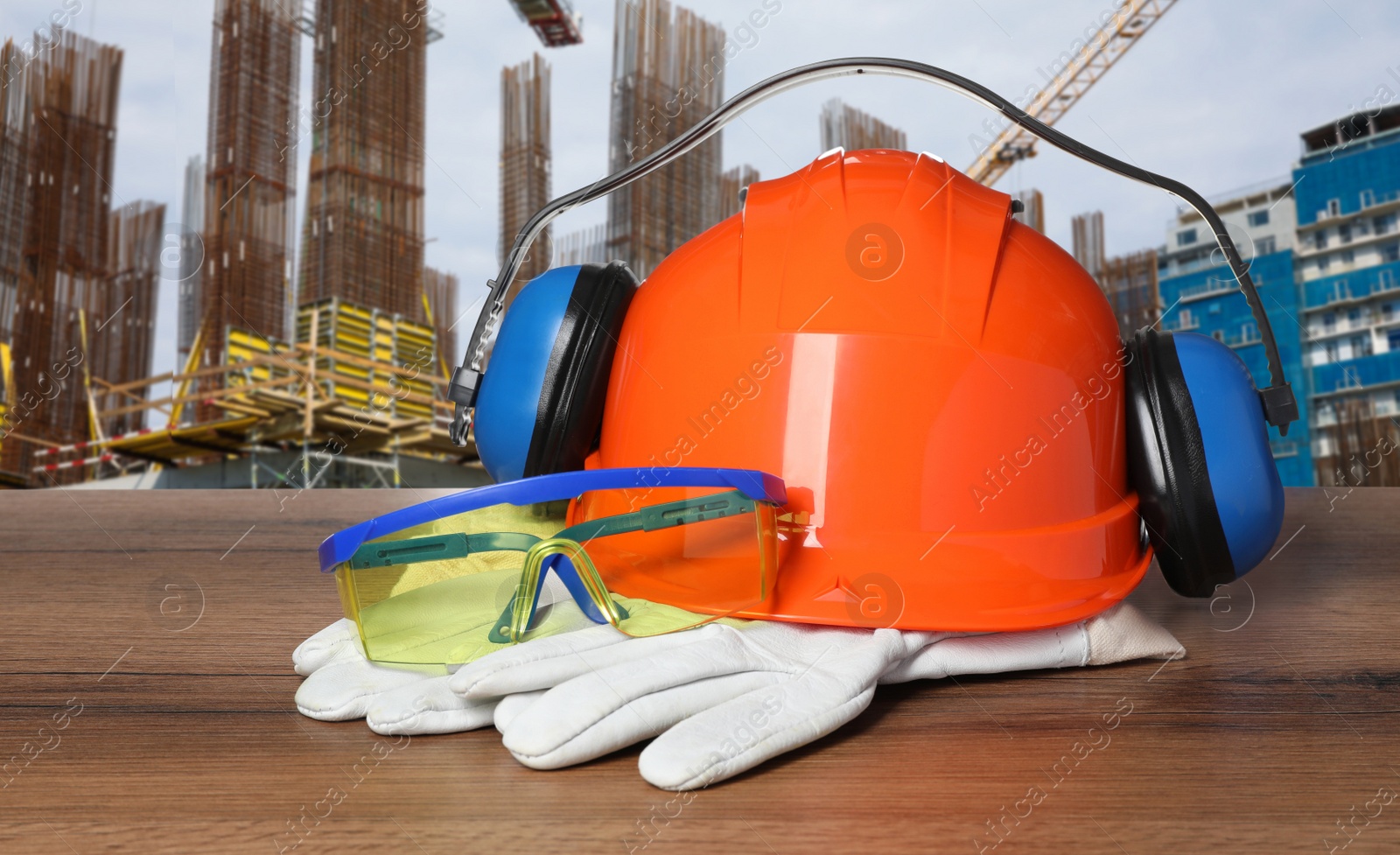 Image of Safety equipment and tools on wooden surface and blurred view of construction site