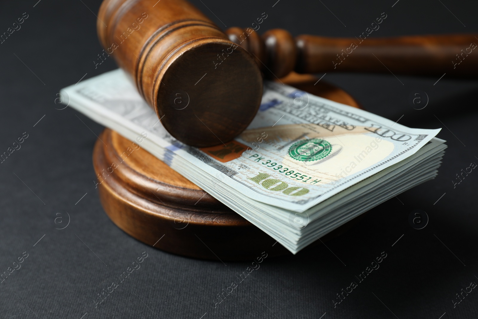 Photo of Law gavel with stack of dollars on black table, closeup