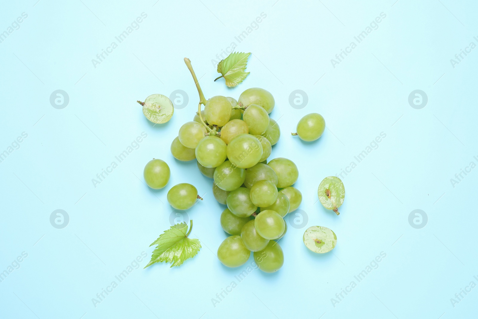 Photo of Bunch of ripe grapes with green leaves on light blue background, flat lay