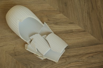 Photo of Broken white ceramic vase on wooden floor, flat lay