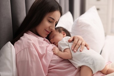 Mother with her sleeping newborn baby in bed indoors