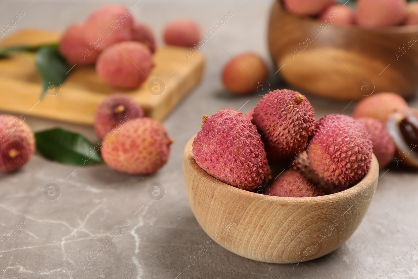 Photo of Fresh ripe lychee fruits in wooden bowl on grey table. Space for text