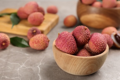 Fresh ripe lychee fruits in wooden bowl on grey table. Space for text