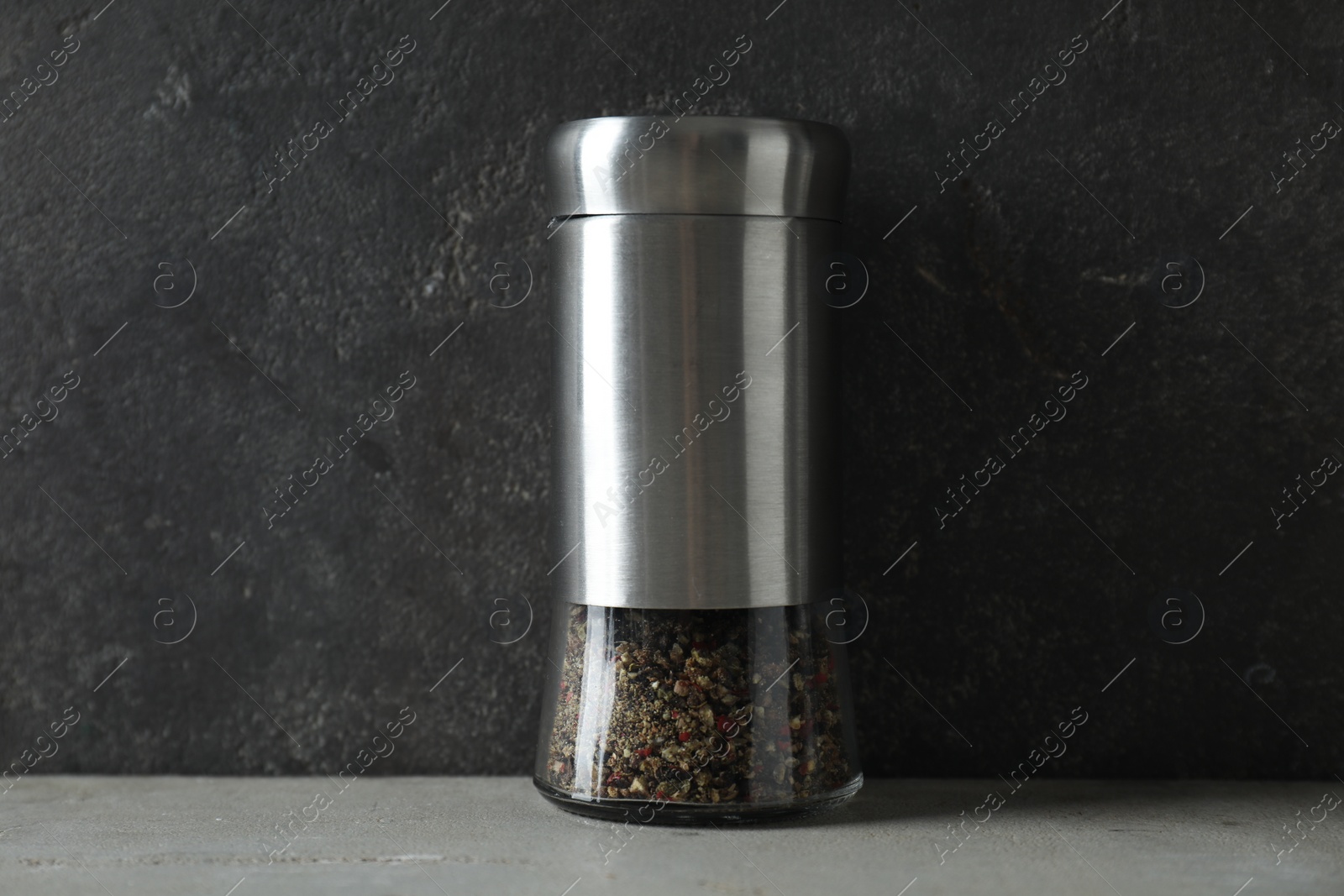 Photo of Pepper shaker on light table against grey background, closeup